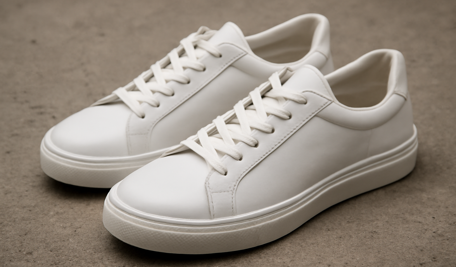 paire de sneakers blanches posées sur sol béton